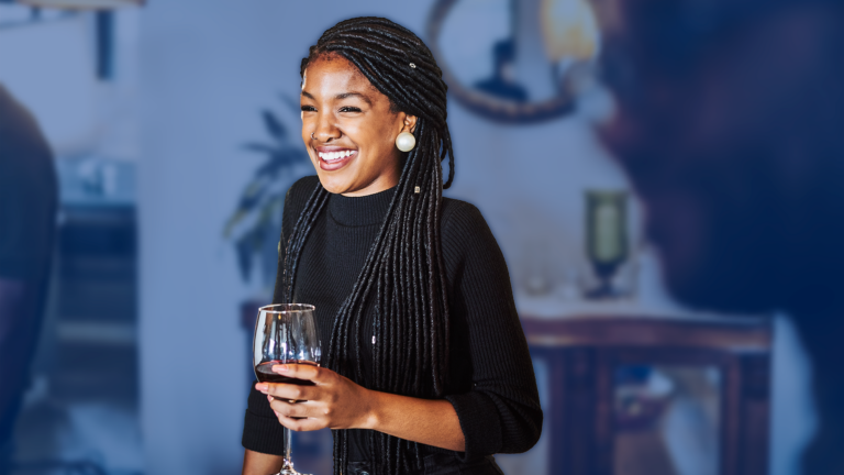 A smiling woman with braided hair holding a wine glass at a social event