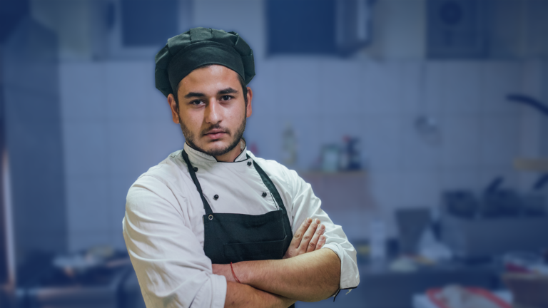 A chef in a kitchen standing with arms crossed